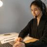 Asian woman using a laptop with a headset in a modern office setting.